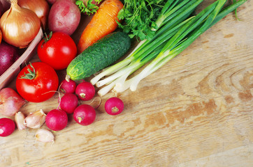 Appetizing vegetables on a wooden table. Green onions, tomatoes, cucumbers, carrots, radishes, garlic, parsley.