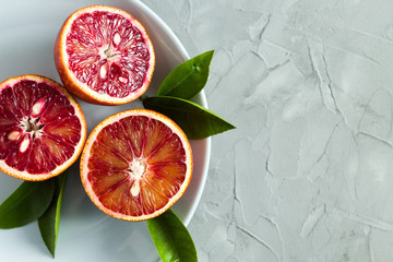 halves of fresh blood oranges with green leaves on a plate on a gray background. copy space. top...