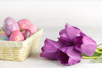 Fototapeta na wymiar Purple tulips and easter eggs on a white wooden table.
