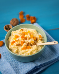 millet porridge with dried apricots and walnuts on a wooden blue background in a bowl