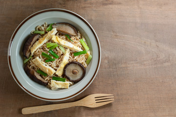 top view of stir fried instant noodle with shiitake mushroom and egg in a ceramic dish on wooden table. asian homemade style food concept.