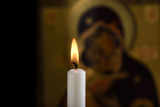 Burning candle in front of the icon of the Mother of God and baby Jesus in the background. Focus on the flame.
