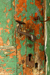 Rusty doorknob and latch on old weathered green door .