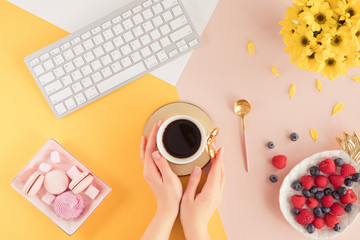 Flat lay of spring and summer female desk with laptop keyboard, cup of tea and yellow flowers on bright background, top view