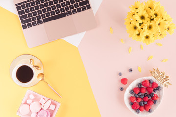 Flat lay of spring and summer female desk with laptop keyboard, cup of tea and yellow flowers on bright background, top view