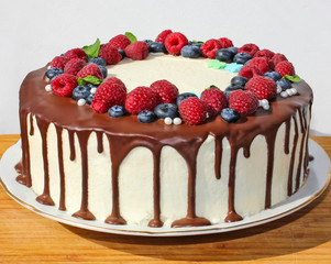 Cake in chocolate, decorated with blueberries, raspberries and green leaves on a white background. Picture for a menu or a confectionery catalog.