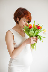 Young pregnant woman in white dress with a bouquet of tulips
