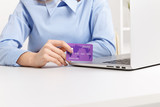 Office woman holding purple credit card and making shopping online at her workplace