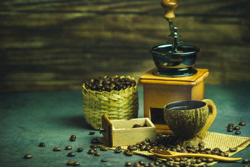 Brew black coffee in coconut cup and morning lighting. Roasted coffee beans in a bamboo basket and wooden spoon. Vintage coffee grinder and pot. Concept of coffee time in morning or start the new day.