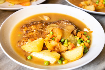 Serving of hainanese chicken chop with gravy, peas, carrots, potatoes.