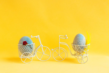 Two Easter eggs ride towards each other on bicycles on a yellow background.