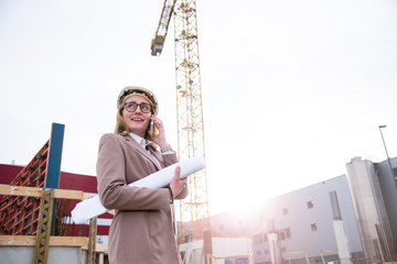 Frau als Architektin mit Helm, Bauplan, Plänen auf einer Baustelle mit Kran