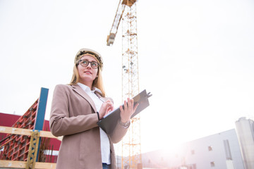 Frau als Architektin mit Helm, Bauplan, Plänen auf einer Baustelle mit Kran