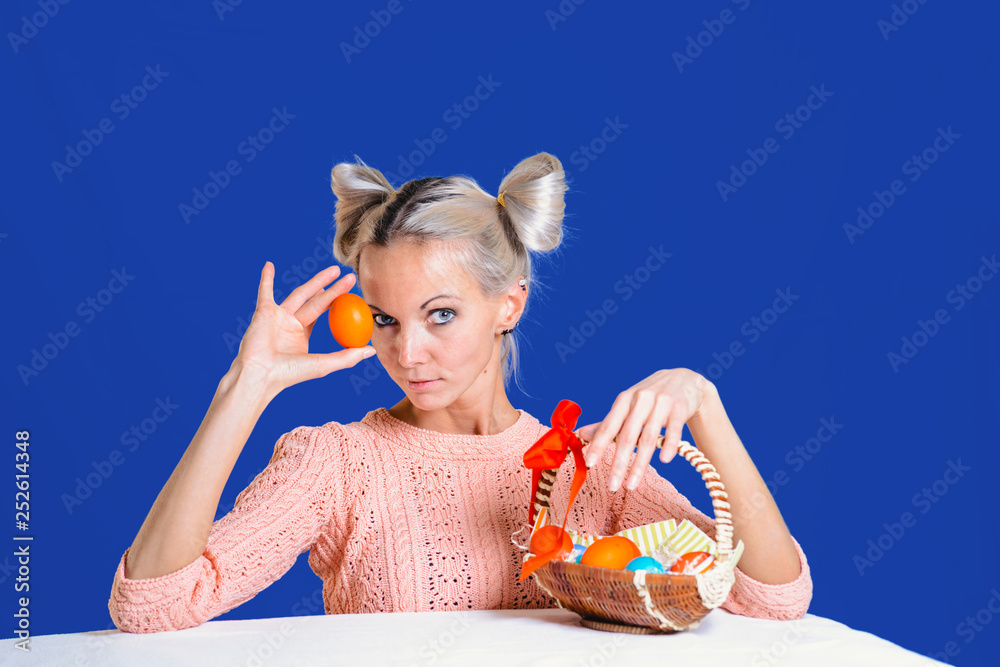 Wall mural Beautiful young girl with basket of Easter eggs on colored background.