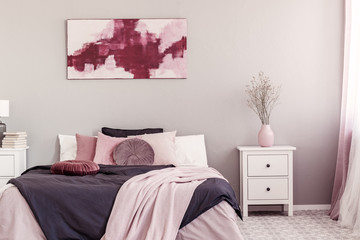 Flower in pastel pink vase on white wooden nightstand next to king size bed in trendy bedroom interior