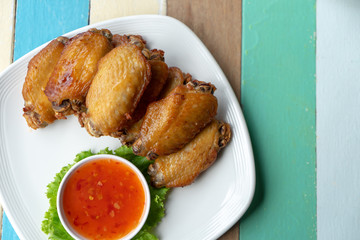 Fried mixed chicken and chicken sauce on white plate over colourful wooden background, top view.