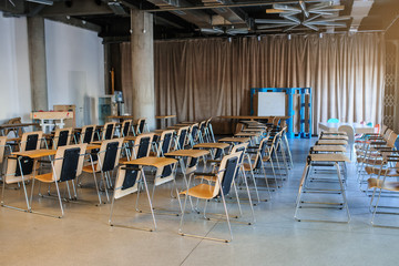 lateral view of a training room/conference hall interior with rows of wood chairs with a small table for each of them