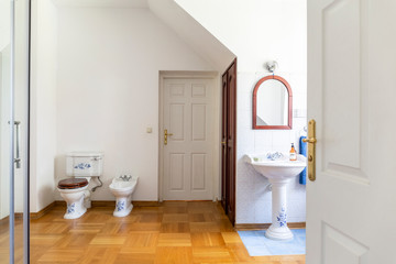 Mirror above whitewash basin in simple bathroom interior with door next to toilet. Real photo