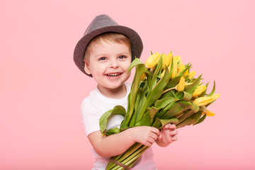 Adorable smiling child with spring flower bouquet looking at camera isolated on pink. Little...