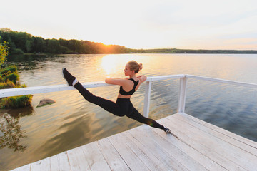 Fototapeta na wymiar Blonde woman doing split on a white wooden pierce at the lake. Barre stretching outdoors