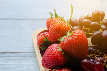 Close up: Selective focus at the top of strawberry. There are many juicy strawberries and red grapes are on yellow wooden plate. Healthy food concept