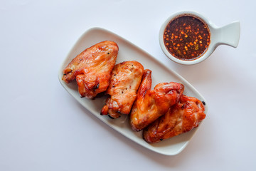 Top view and close up: juicy grilled chicken wing on white plate and spicy Thai Style sauce on white background. Recommend menu with papaya salad(SOM TUM) famous and popular food.
