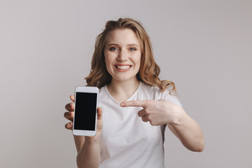 Handsopme young woman holding white iphone isolated over the white background.