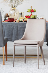 Stylish beige chair in front of dining room table set with food and fruits