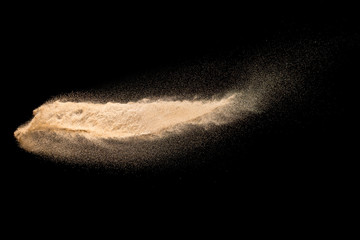 Dry river sand explosion. Brown color sand splash against black background. Yellow sand fly wave in...