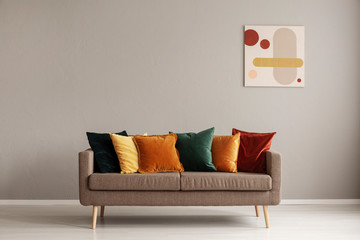 Abstract painting on grey wall of retro living room interior with beige sofa with pillows