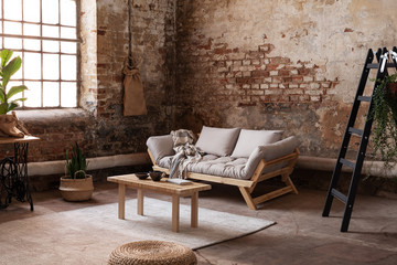 Black ladder next to couch and wooden table in industrial flat interior with plants and window....