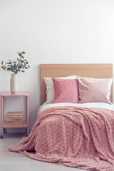 Pink pillows and cozy blanket on single bed in elegant hotel room, copy space on empty white wall