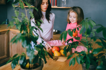 Adorable young woman playing with her little funny daughter in kitchen. Portrait of pretty mother and her child building rower with plastic fruits. Happy female family indoor lifestyle portrait.