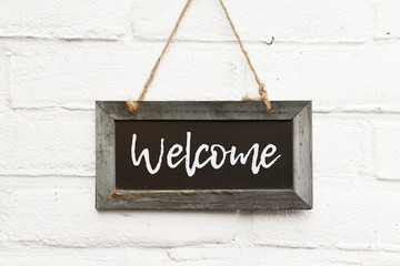 Text welcome hello come in sign on wooden blackboard hanging on outdoor wall