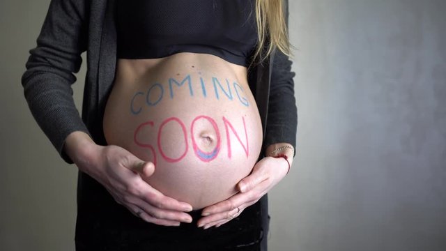 Pregnant woman with an inscription coming soon on her belly. 4K