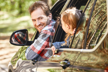 To travel is to live. Father and daughter looking out the car window and smiling happily to each...