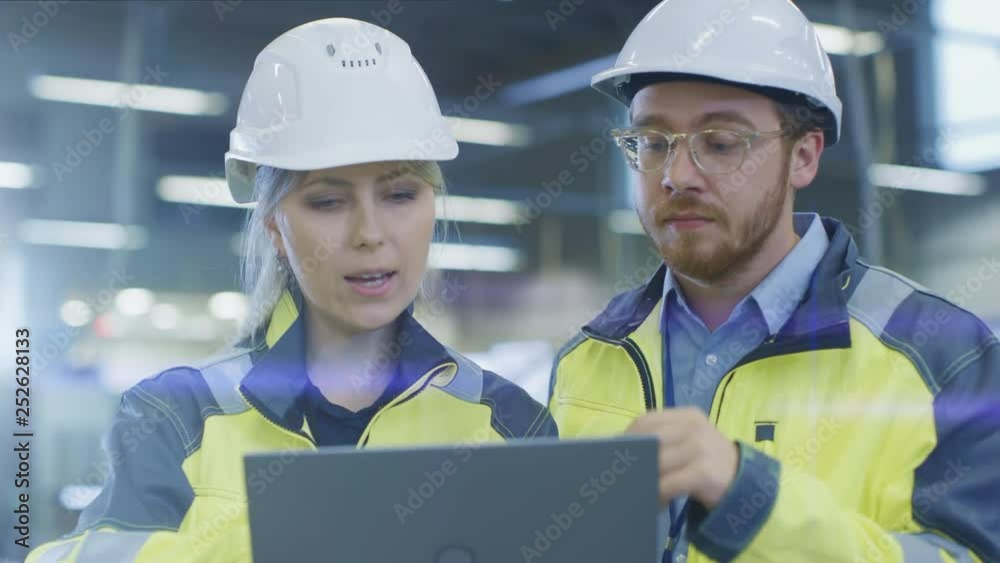 Poster At the Factory: Male Mechanical Engineer Holds Component and Female Chief Engineer Work on Personal Computer, They Discuss Details of the 3D Engine Model Design for Robotic Arm.