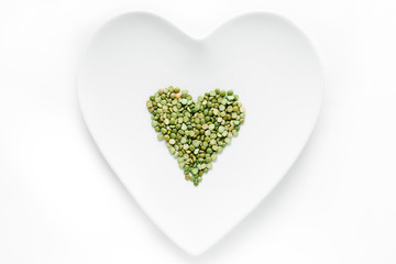 Green dry peas lie in the shape of a heart on a white plate
