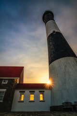 The sun setting behind a lighthouse as golden light shines through its windows. Sun burst and rays...