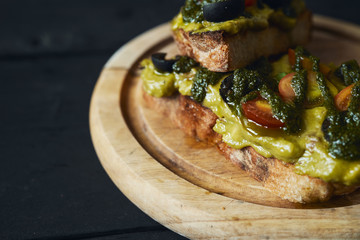 Fresh avocado toast with spices on wooden cut board on dark background