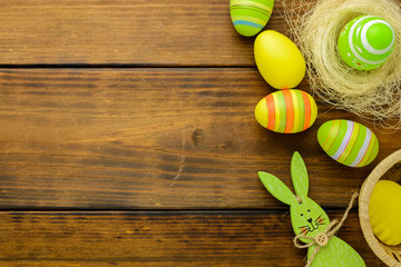 Green and yellow Easter eggs in a nest on a brown wooden table. Top view, copy space.