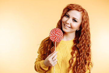 Beautiful young curly redhead woman holding a red white lollipop and smiling