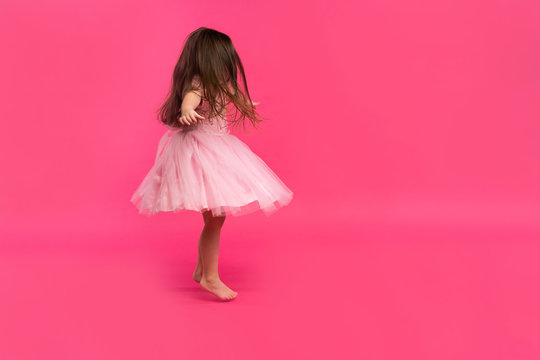 Cute little girl dreams of becoming a ballerina. Little Dancing Girl. Studio Shoot Over Pink Background