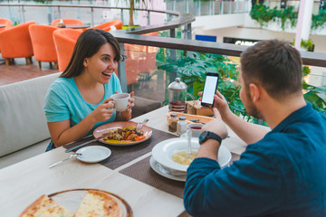 couple eating in cafe. man show phone screen. white copy space
