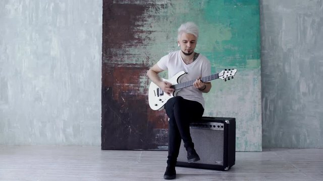 Blonde guy sitting and playing the guitar