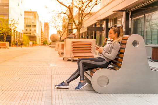 An athletic woman sitting on a bench and using her smartphone