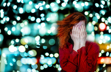 A woman covers her face with her hands. It is surrounded by bright lights.