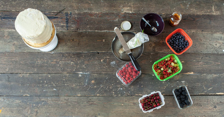 white cream cake base near boxes with berries and other decor on old wooden table, top view