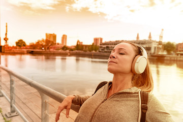 An athletic woman listening to music next to the bridge railing