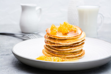Delicious homemade pancakes with tangerines and honey, glass of milk on a plate on the table